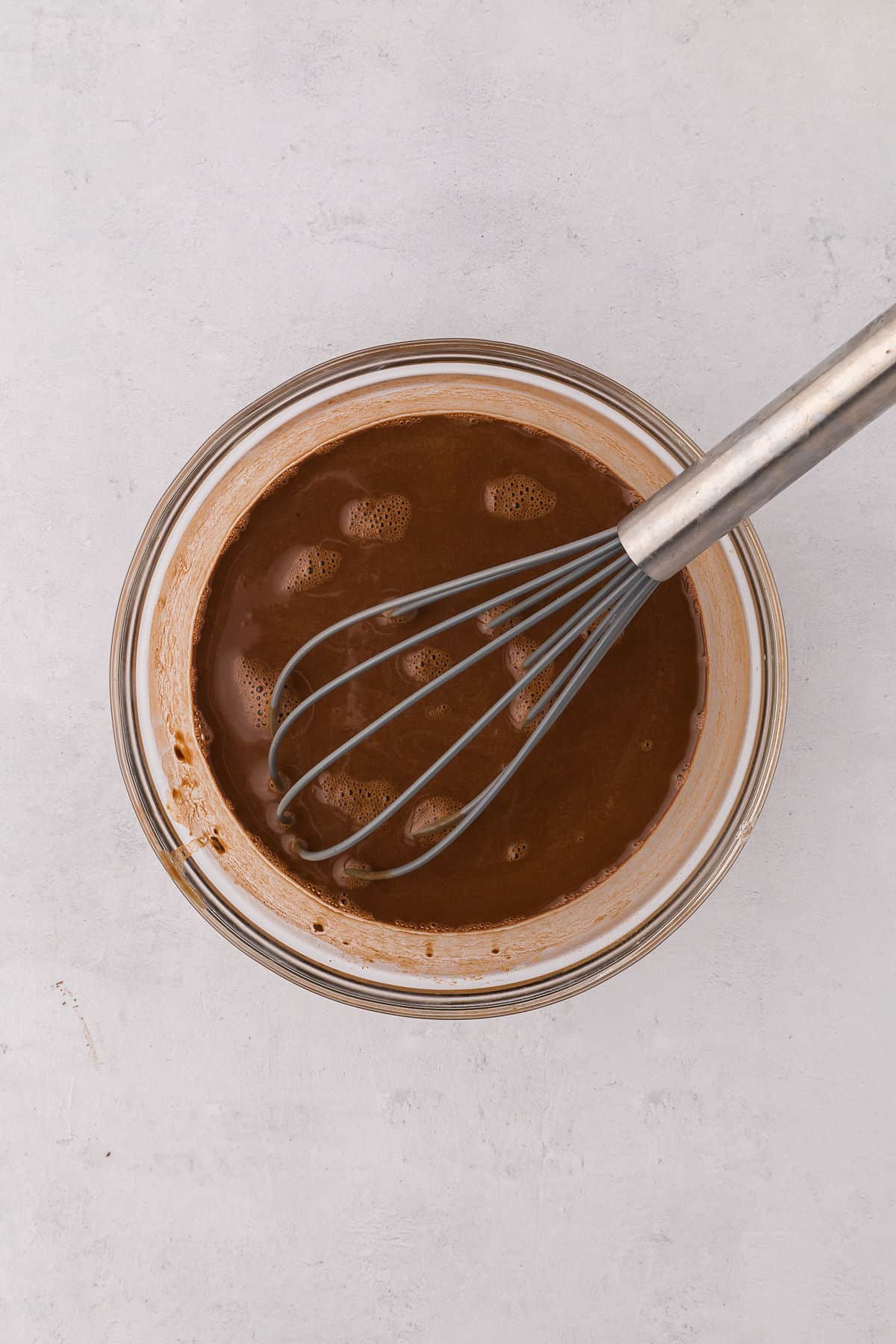 Hot water mixed with cocoa, instant coffee and dash of salt in a glass bowl on white countertop being whisked.