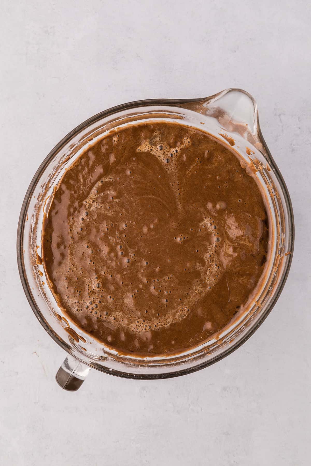 Chocolate birthday cake batter in a glass mixing bowl on white countertop