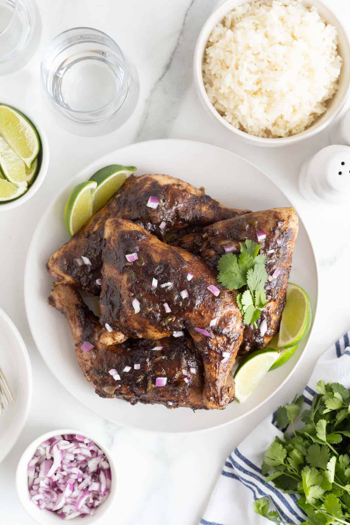 Overhead shot of Jamaican jerk chicken on a white plate with lime wedges and a side of white rice