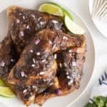 Closeup of Jamaican jerk chicken leg quarters topped with red onion, lime wedges on the side