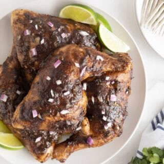 Closeup of Jamaican jerk chicken leg quarters topped with red onion, lime wedges on the side