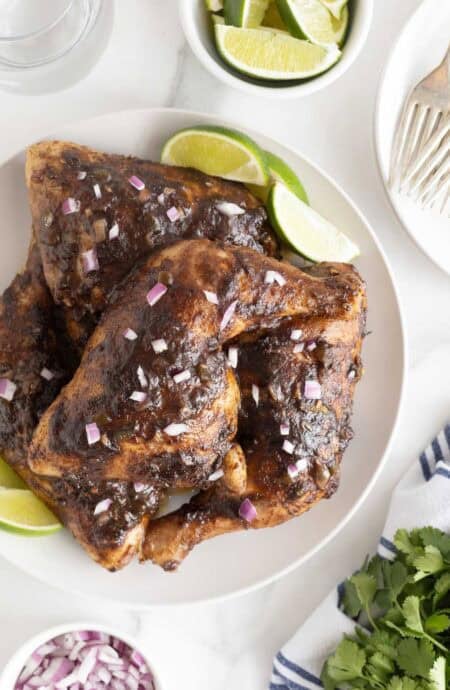 Closeup of Jamaican jerk chicken leg quarters topped with red onion, lime wedges on the side