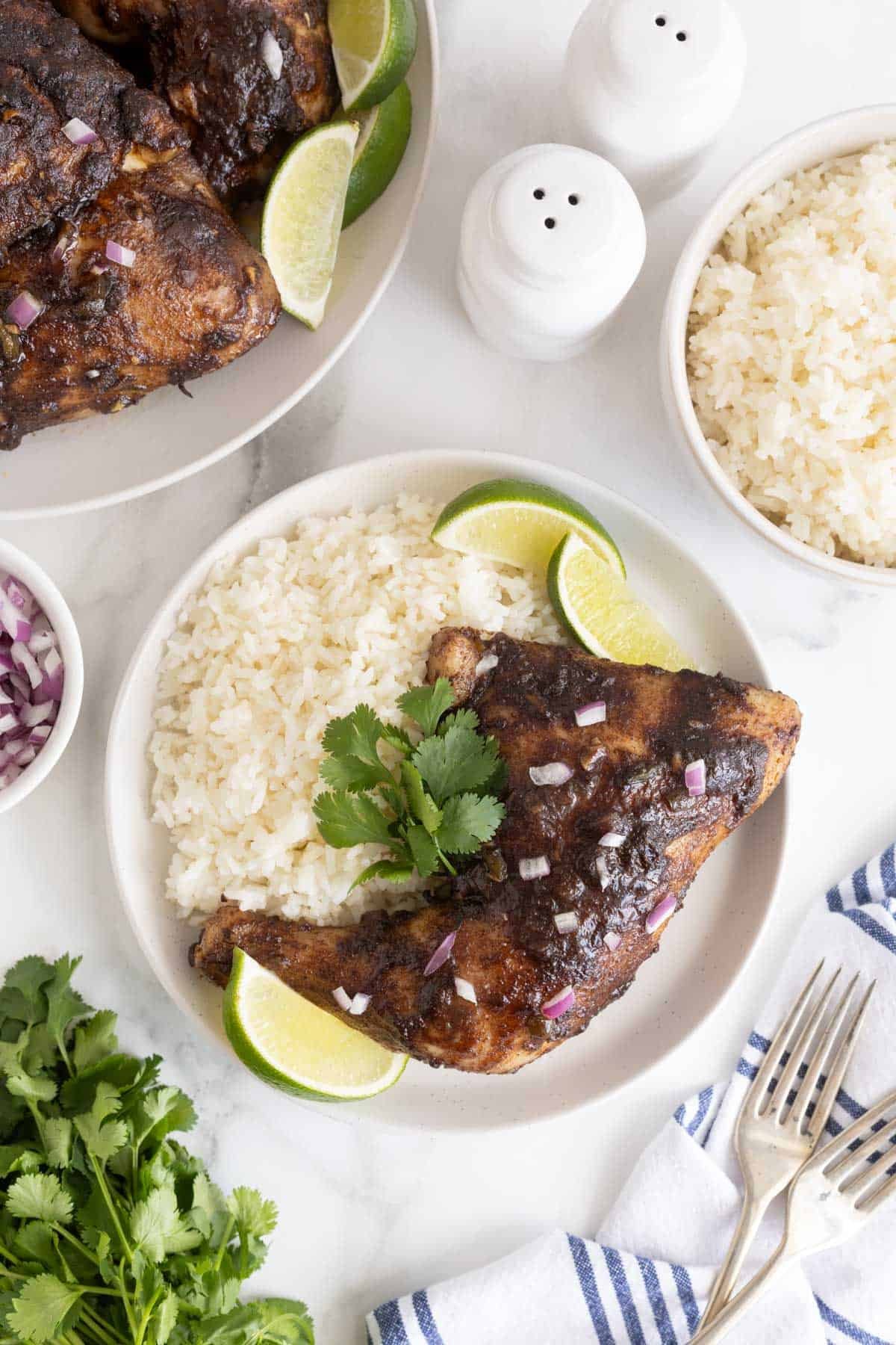 Overhead shot of a plate with Jamaican jerk chicken, white rice, cilantro, and lime wedges, surrounded by ingredients