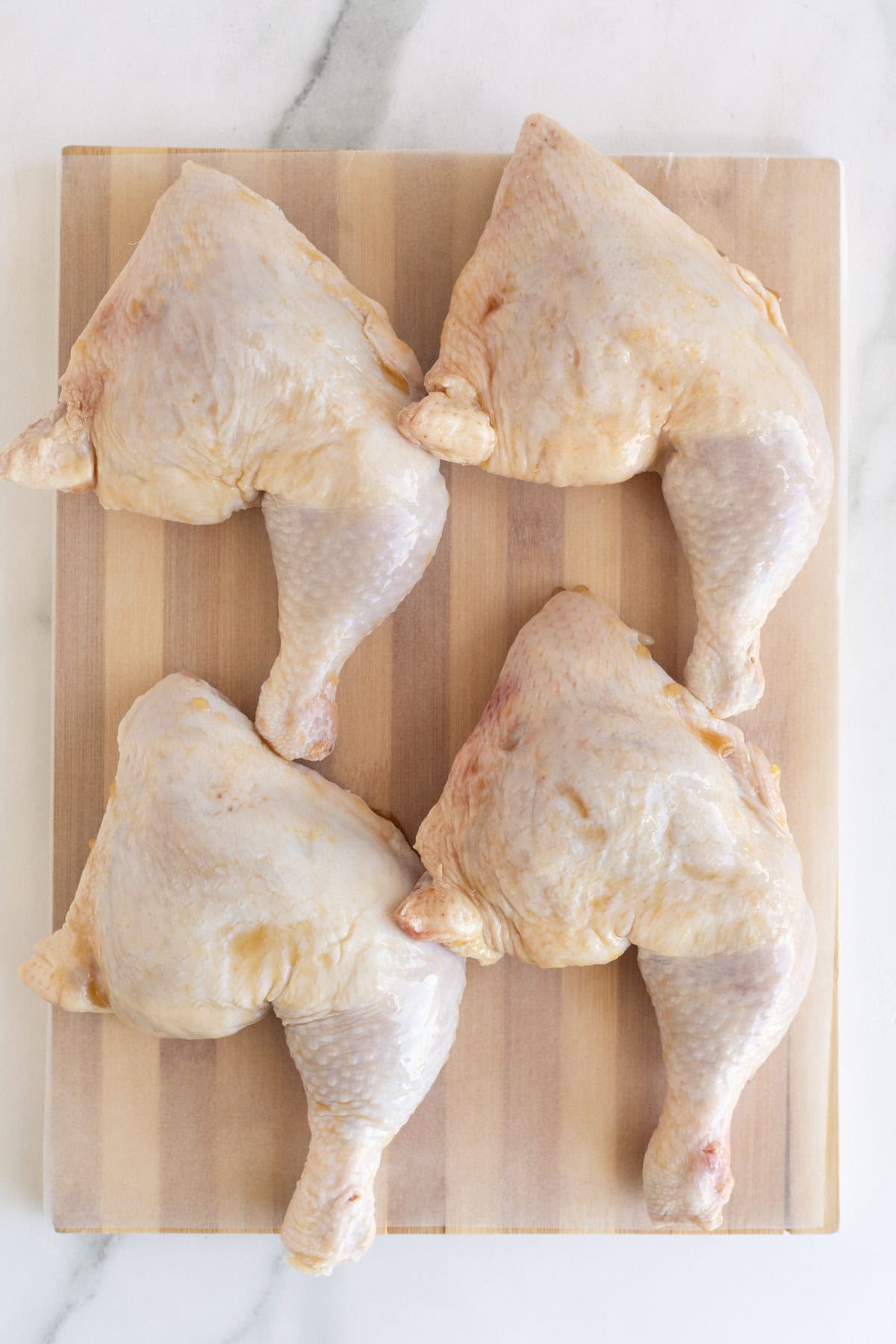 Raw chicken leg quarters coated with red palm oil, arranged on a wooden cutting board