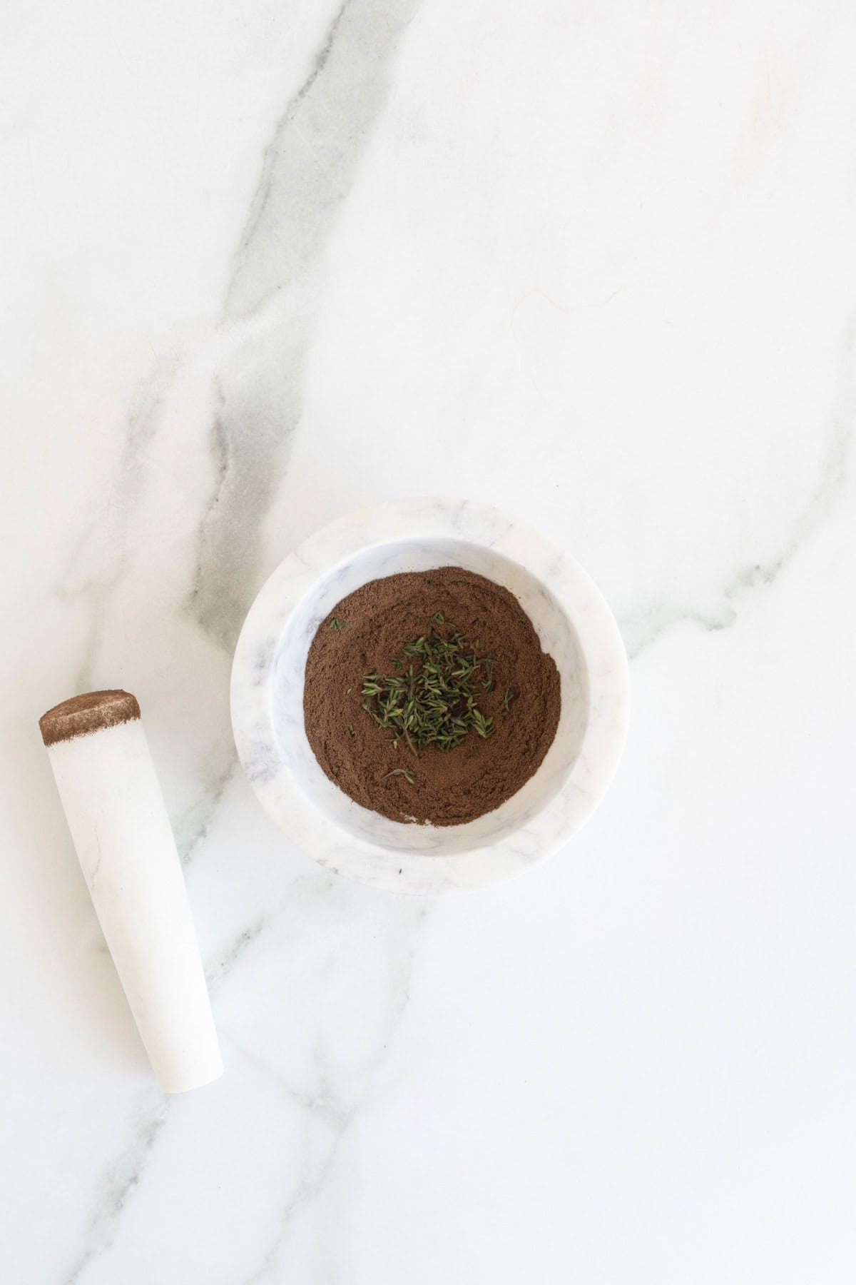 Ground allspice and fresh thyme in a marble mortar with pestle on the side