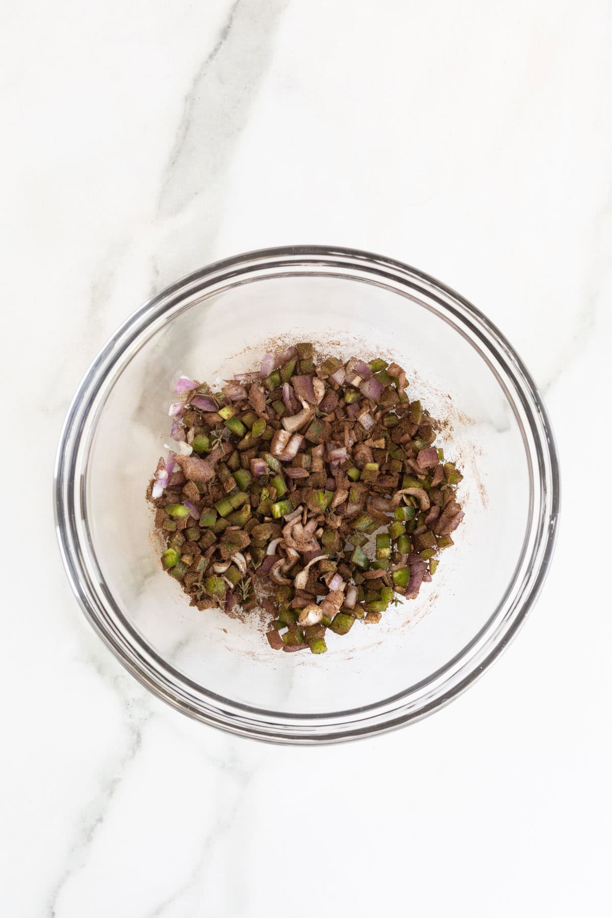 Combined jerk marinade ingredients in a bowl with spices and chopped vegetables