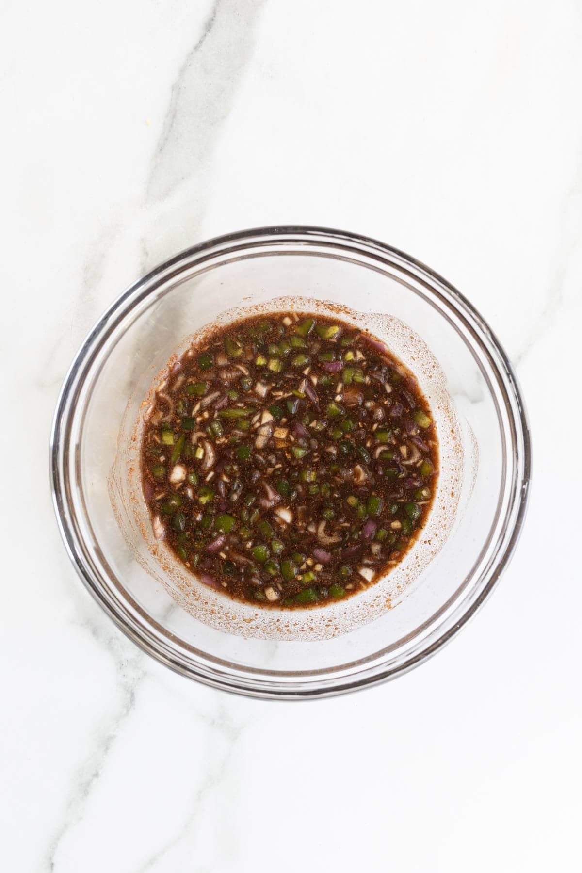 Fully mixed jerk marinade with diced vegetables in a glass bowl