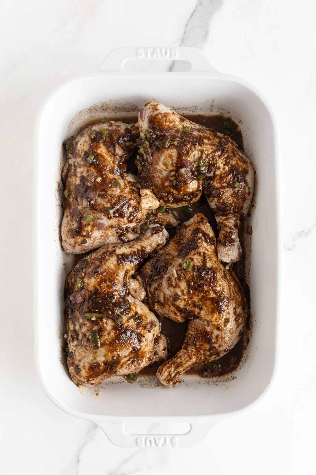 Chicken leg quarters coated in jerk marinade and arranged in a white baking dish
