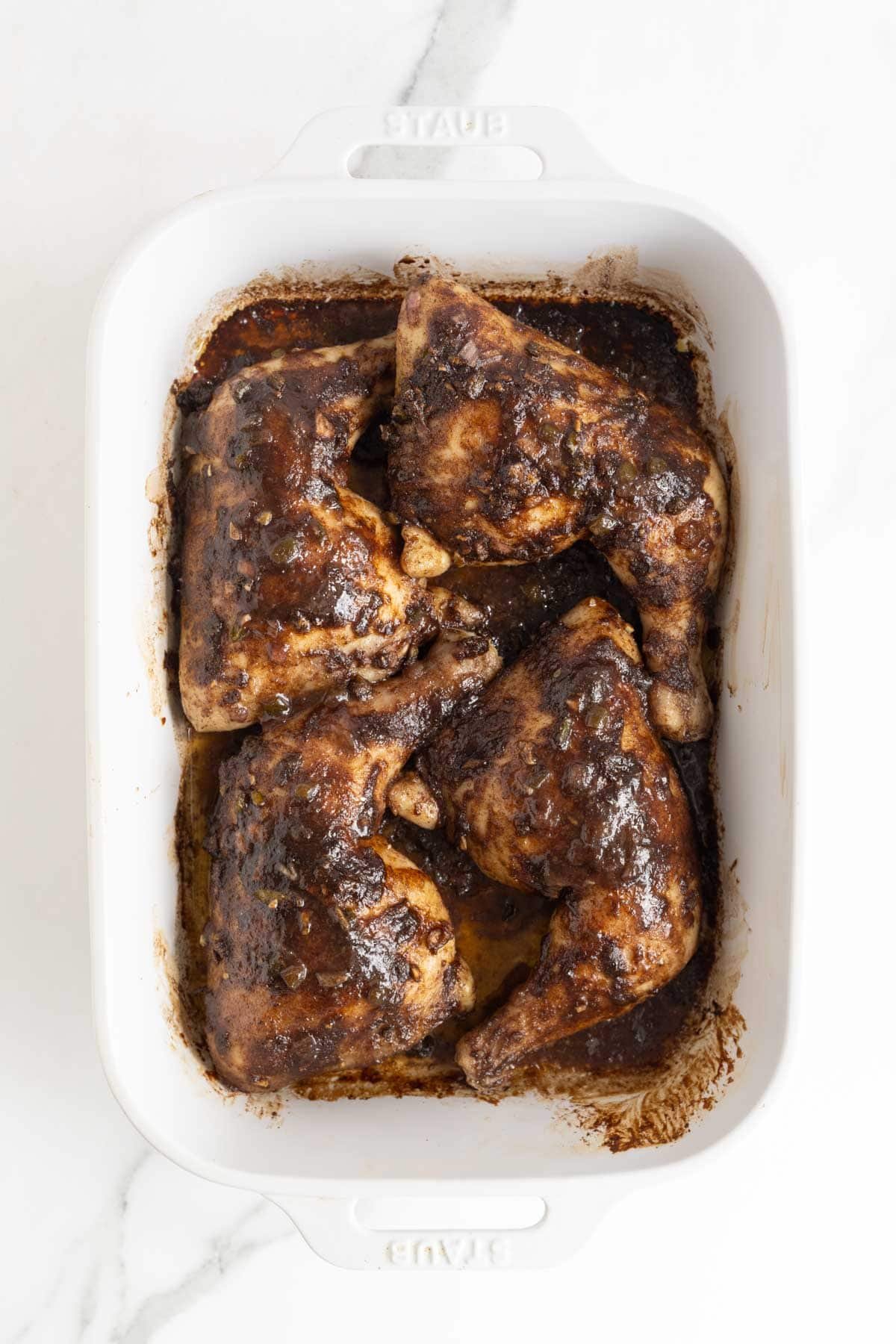 Baked Jamaican jerk chicken in a white dish with rich, dark marinade coating each piece