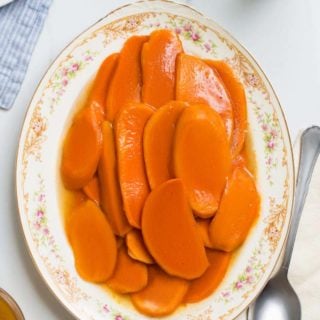An overhead shot of Candied Sweet Potatoes on a vintage white platter against a white background