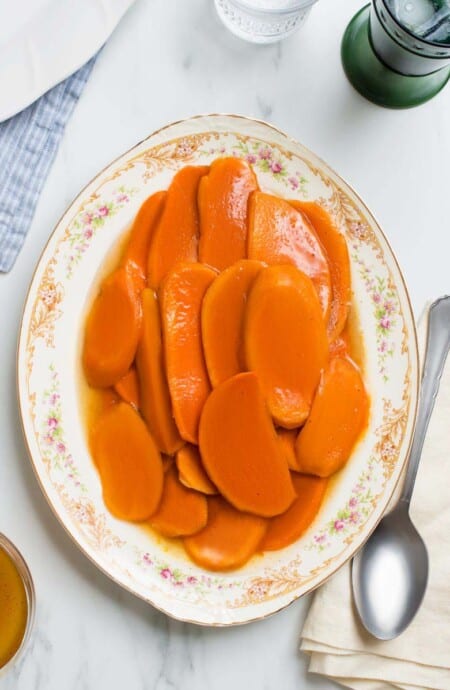 An overhead shot of Candied Sweet Potatoes on a vintage white platter against a white background