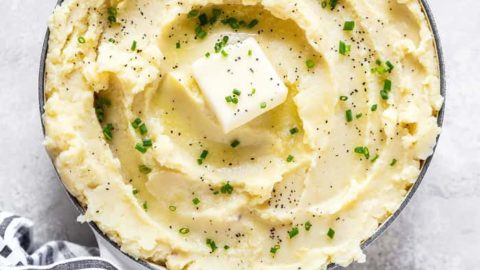 An overhead of a large bowl of creamy buttery Garlic Mashed Potatoes Recipe against a white background with striped napkin