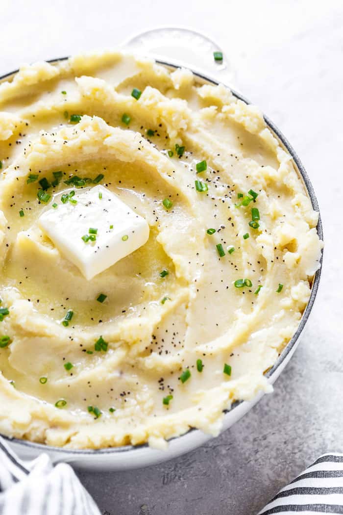 A close up of large bowl of roasted garlic mashed potatoes with pats of butter and parsley