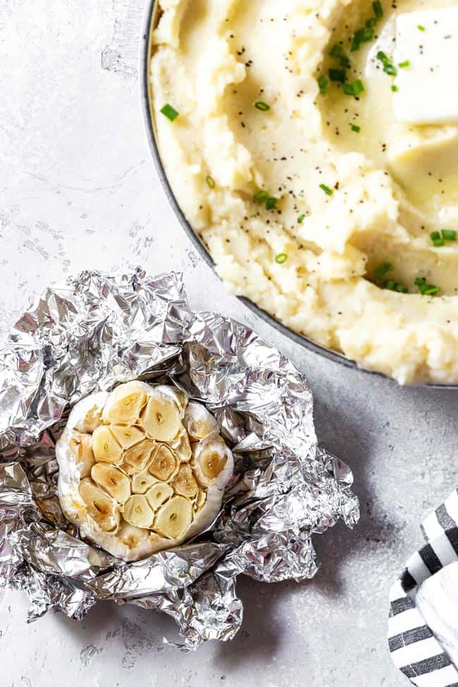 Roasted garlic in foil next to garlic mashed potatoes recipe