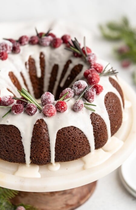 A close up of Gingerbread bundt cake with white glaze on white cake plate