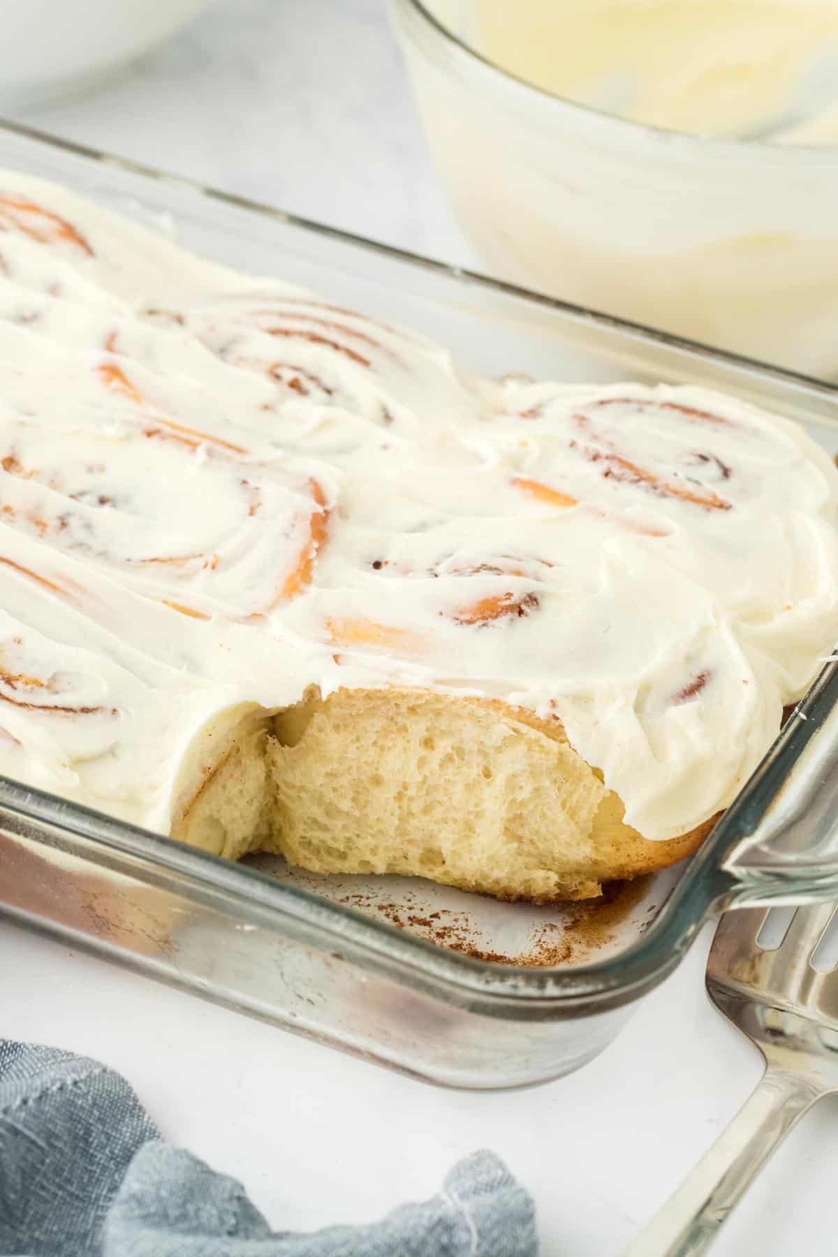 A baking dish filled with homemade cinnamon rolls, with one roll removed, showing the soft texture inside the dish