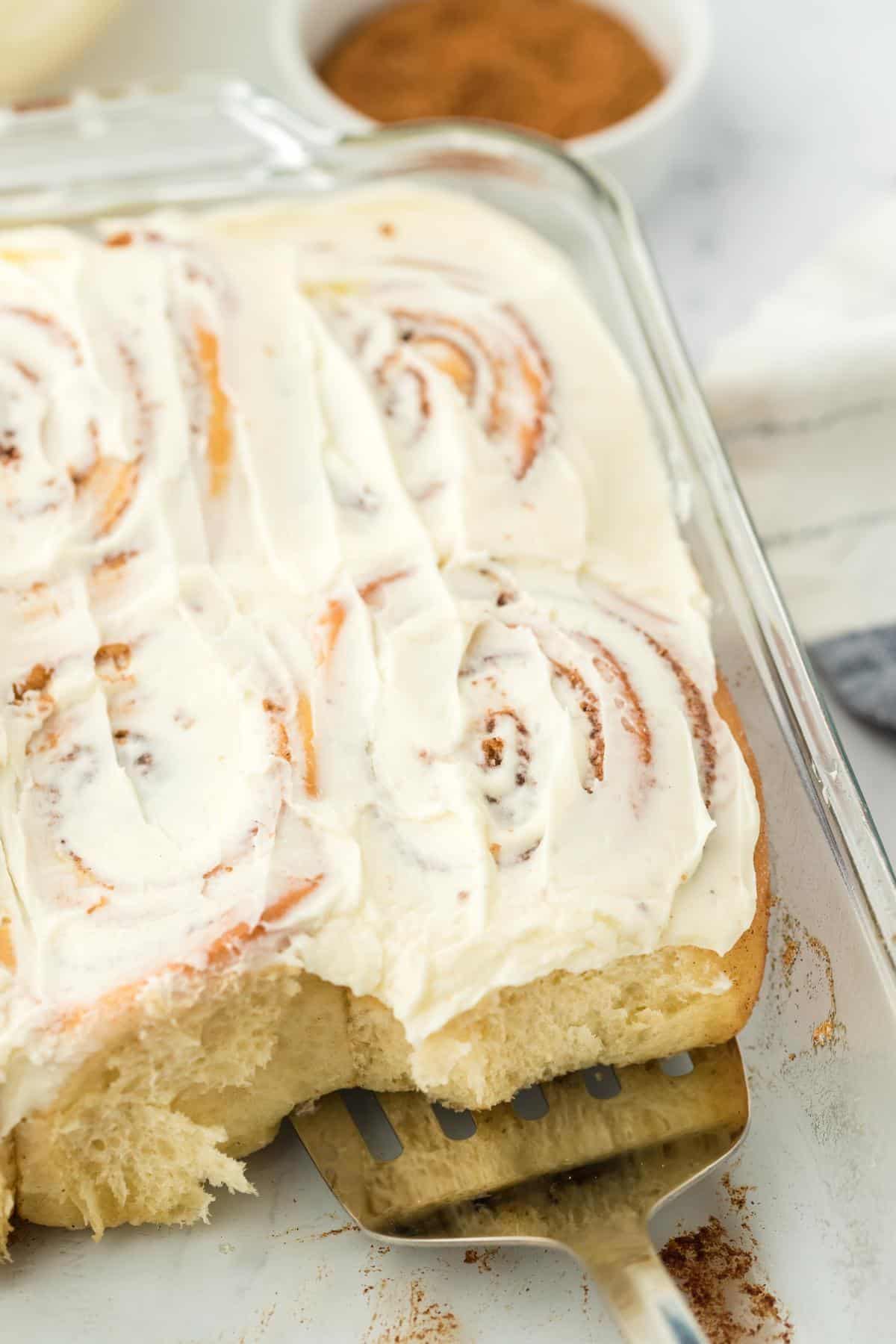 A closeup of a spatula holding a homemade cinnamon roll on a baking dish, showcasing its fluffy texture and swirled filling