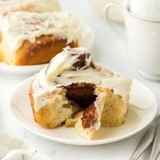 A homemade cinnamon roll on a white plate ready to serve