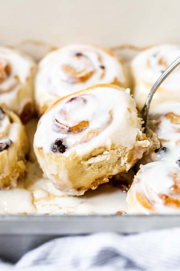 A homemade cinnamon roll being lifted out of a baking pan
