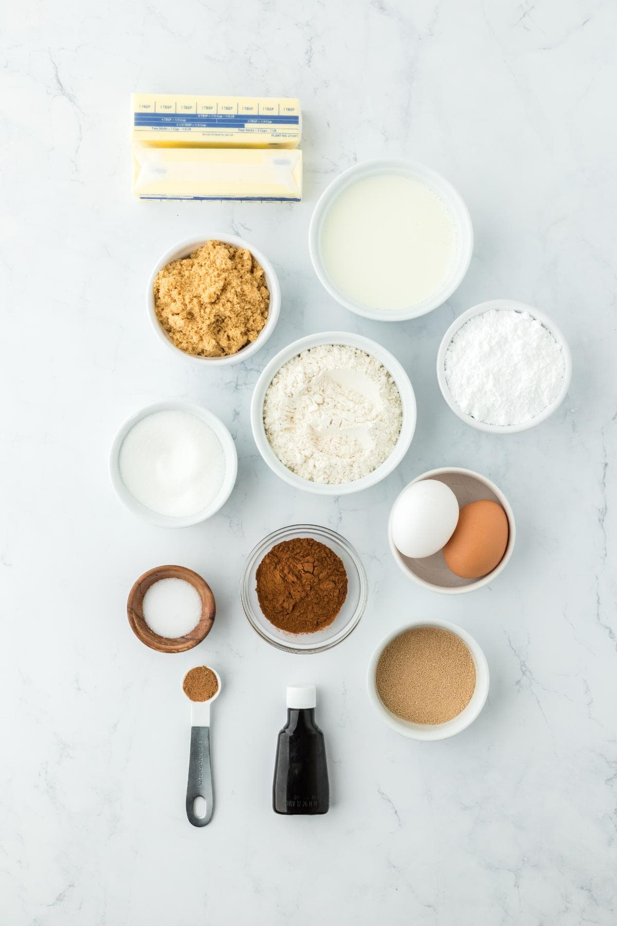 Overhead shot of ingredients for making homemade cinnamon rolls on a white surface before mixing