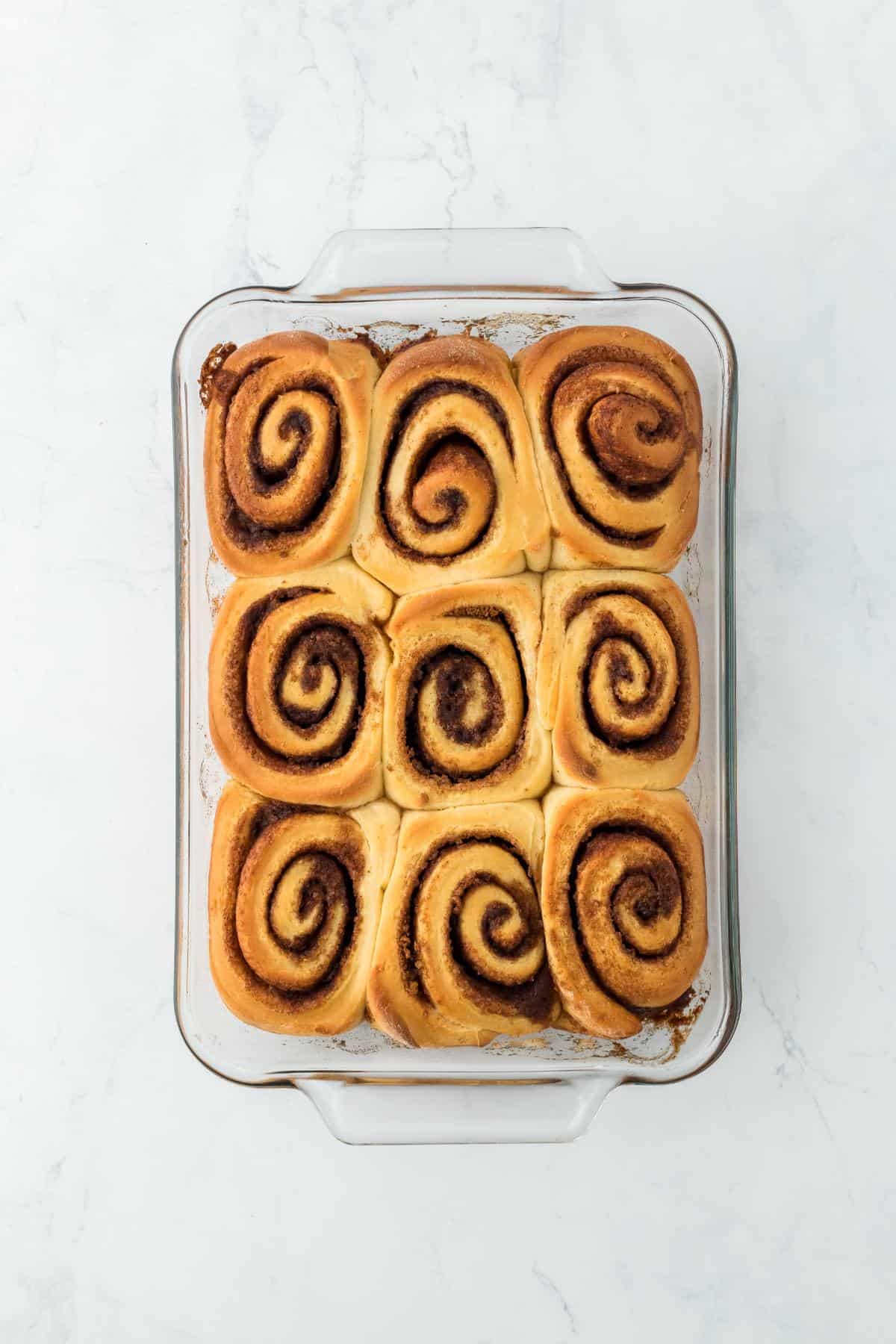 Baked cinnamon rolls in a glass dish with a golden-brown surface