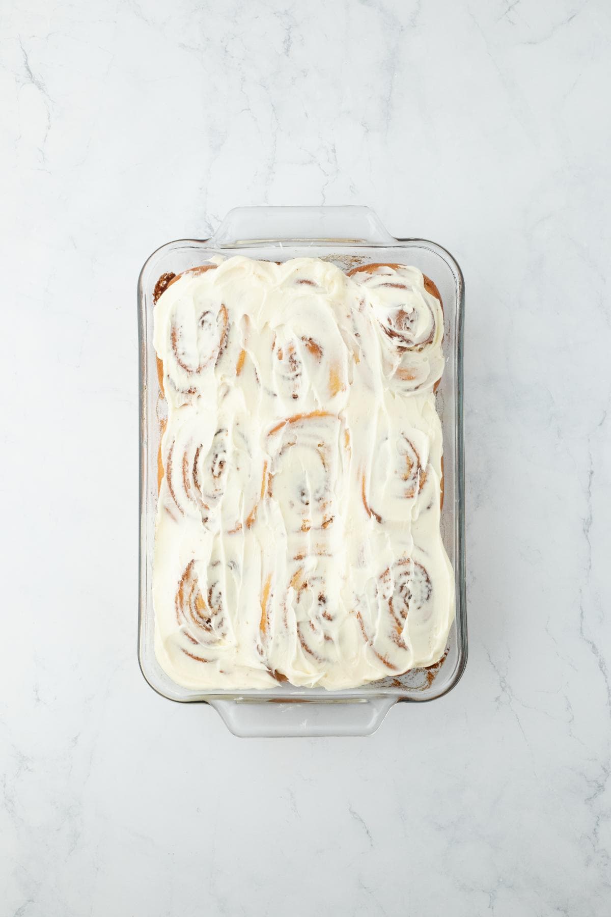 Homemade cinnamon rolls generously frosted with icing in the baking dish, ready to serve