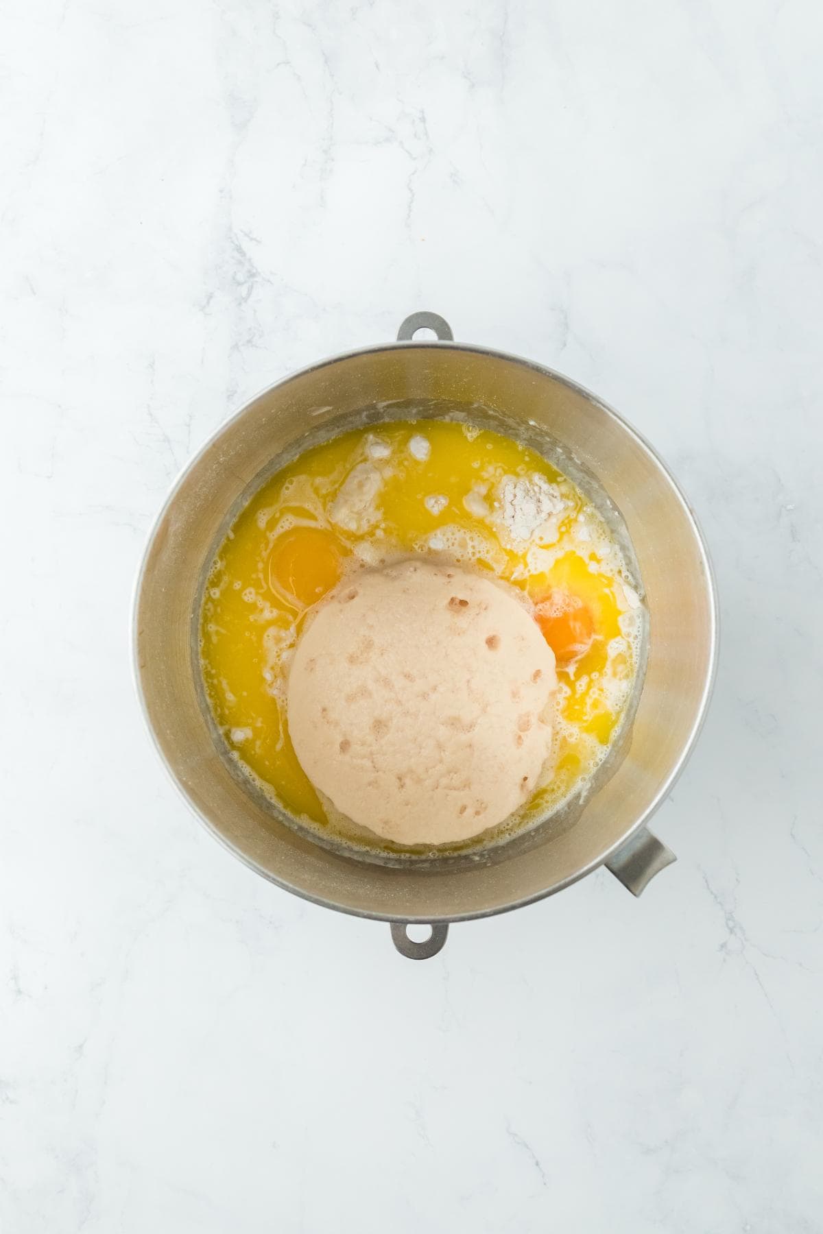 A mixing bowl with eggs, melted butter, and proofed yeast on top of dry ingredients