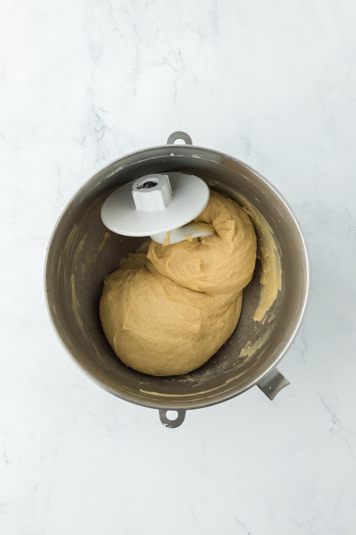 A mixing bowl with smooth dough formed and wrapped around a dough hook