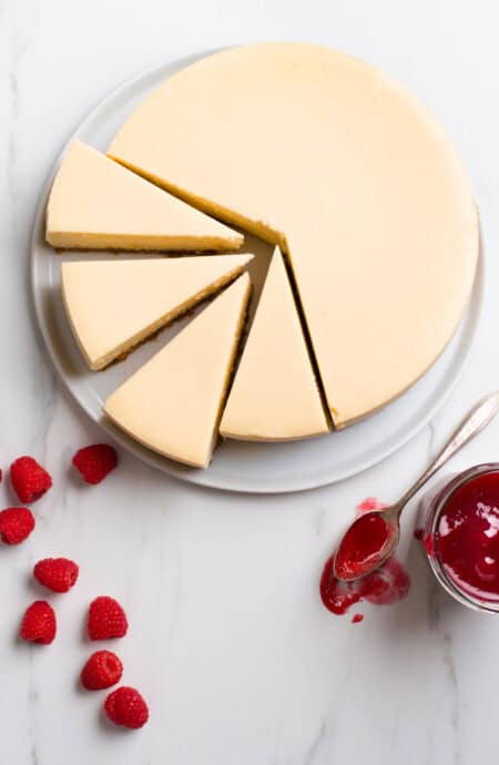 New York Cheesecake overhead shot with full cheesecake and four slices with raspberries and raspberry sauce