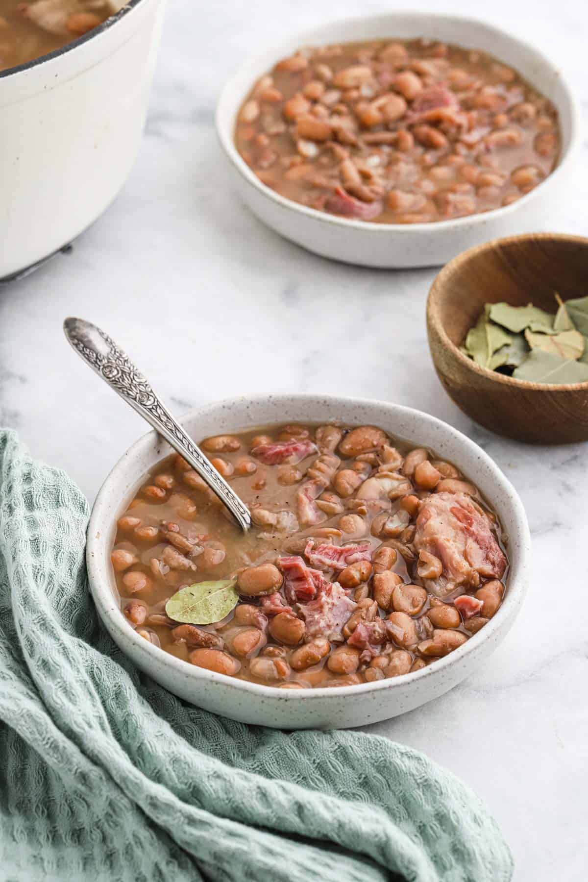 Overhead shot of a large white bowl of pinto beans with ham hock and bay leaf