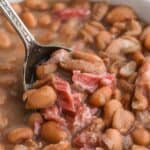 A overhead shot of a big pot of pinto beans, ham hock and bay leaves against white background