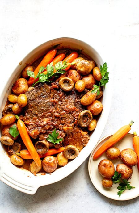 Overhead shot of delicious Pot Roast recipe with carrots, potatoes and parsley against white background