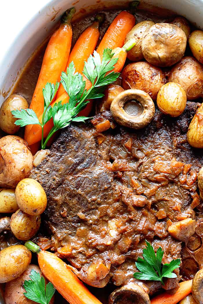 Close up of pot roast in a white casserole dish with mushrooms and carrots