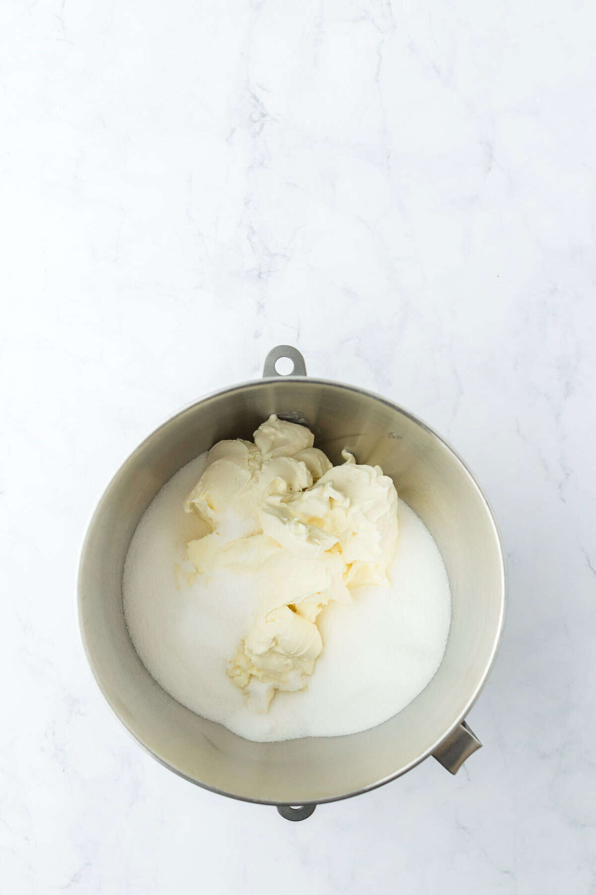 Cream cheese and sugar in a stand mixer bowl on white countertop