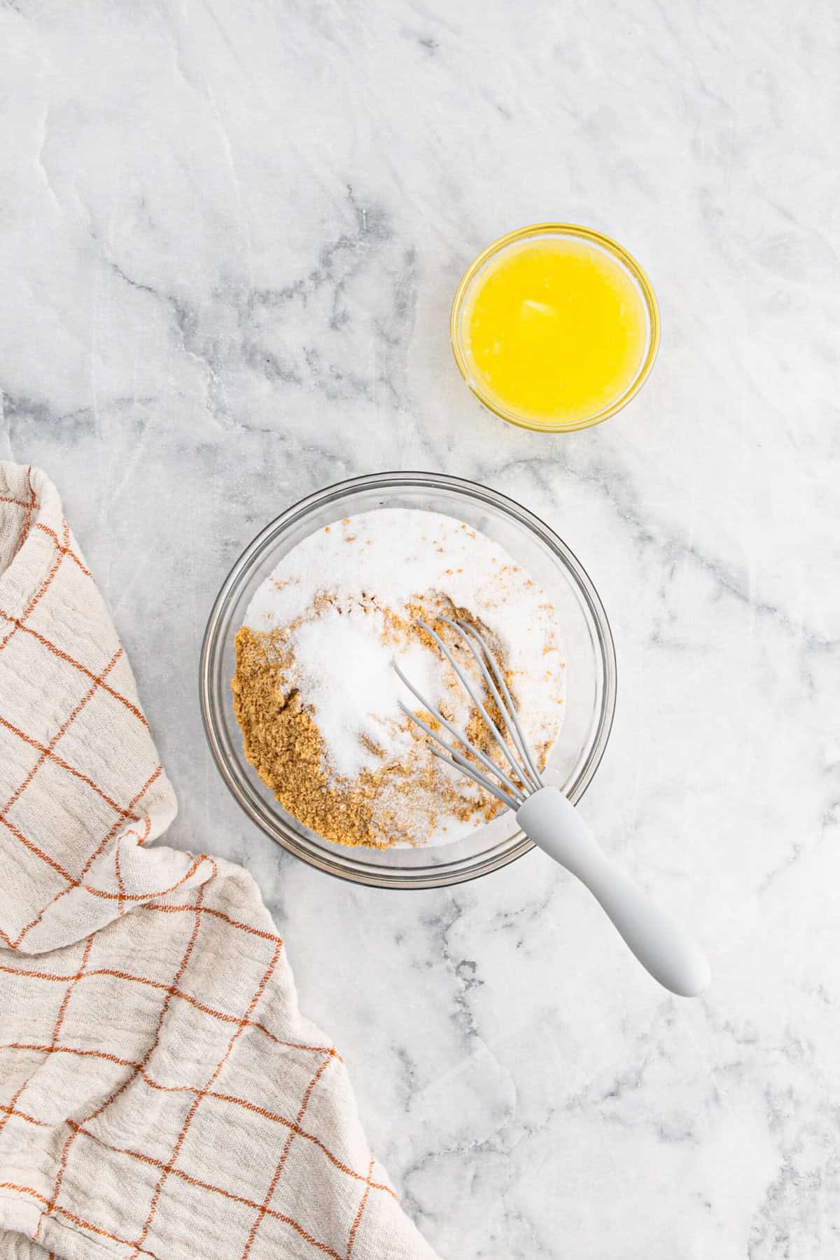 Sugar and graham cracker crumbs in a glass bowl with melted butter on white countertop