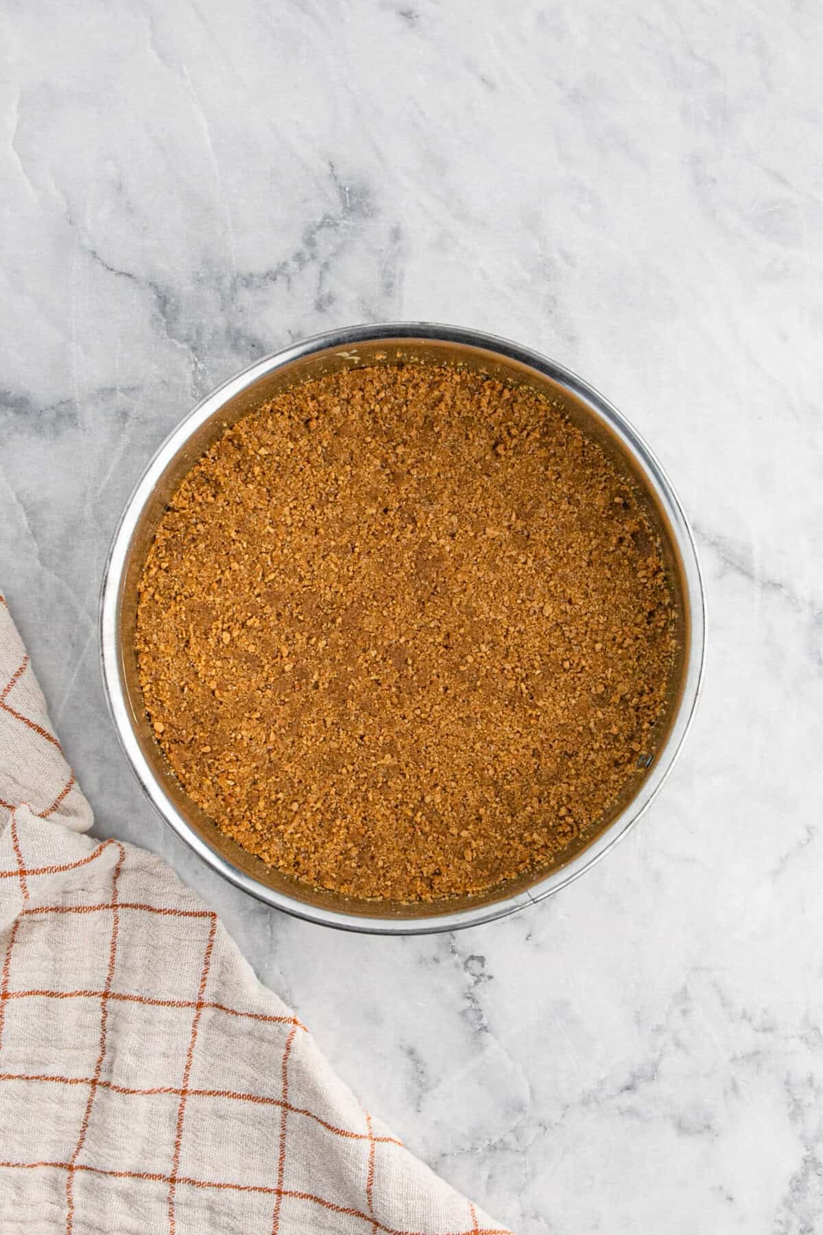 Graham cracker mixture pressed into springform pan on white countertop