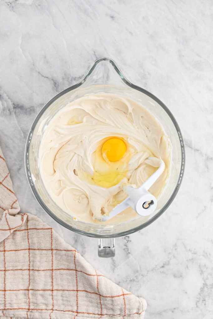 Eggs added to cheesecake mixture in stand mixer on white countertop