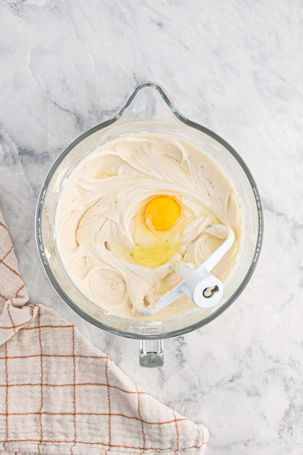 Eggs added to cheesecake mixture in stand mixer on white countertop