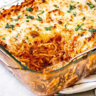 Baked spaghetti casserole dug into and added to a plate on gray background