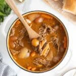 A large dutch oven filled with classic pot roast ready to enjoy with a wooden spoon digging in