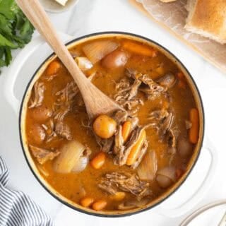 A large dutch oven filled with classic pot roast ready to enjoy with a wooden spoon digging in