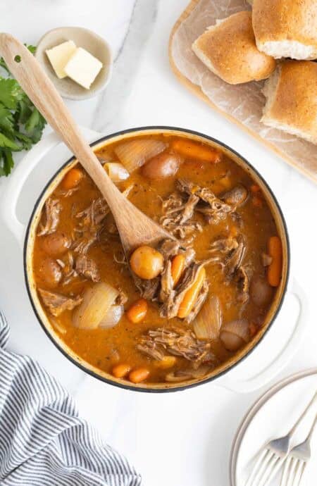 A large dutch oven filled with classic pot roast ready to enjoy with a wooden spoon digging in