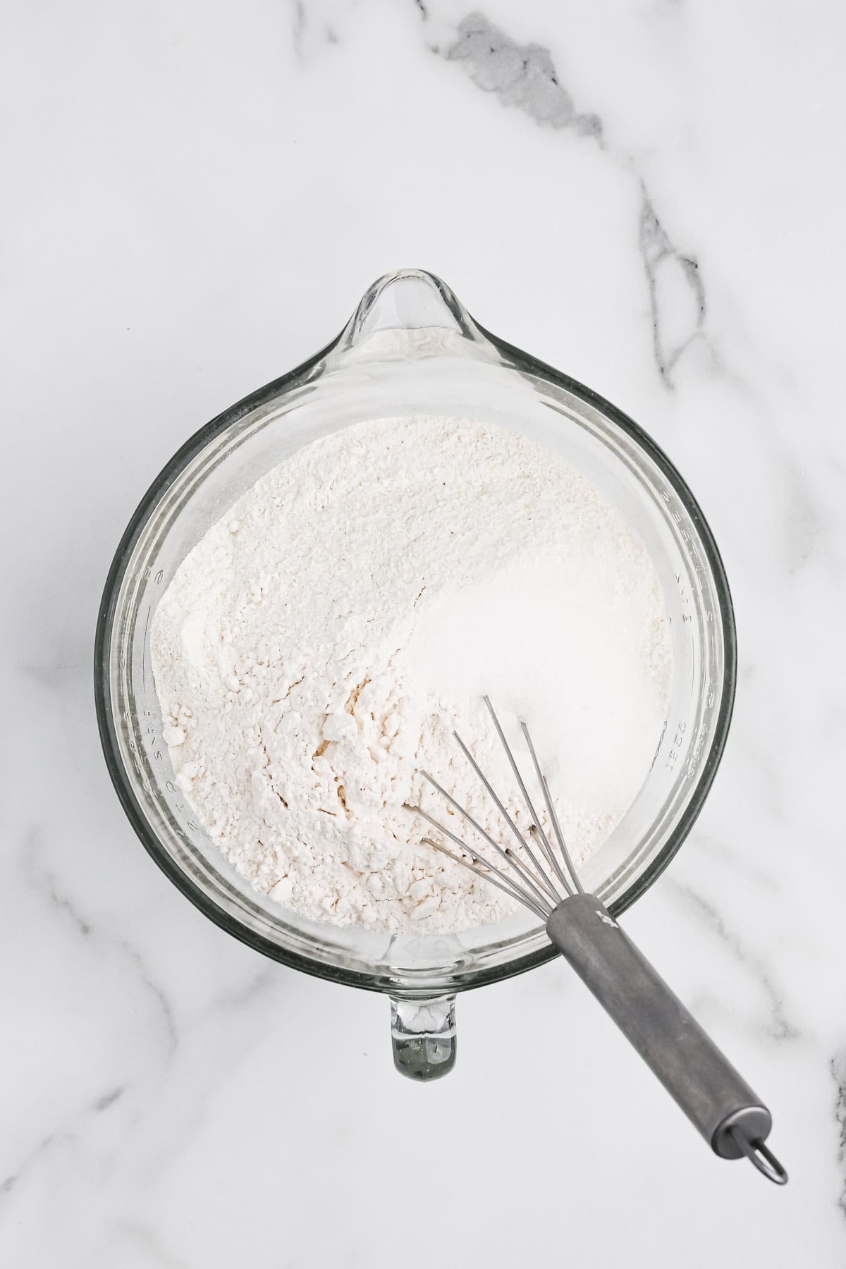 Cornmeal, flour and dry ingredients in a clear mixing bowl on white background