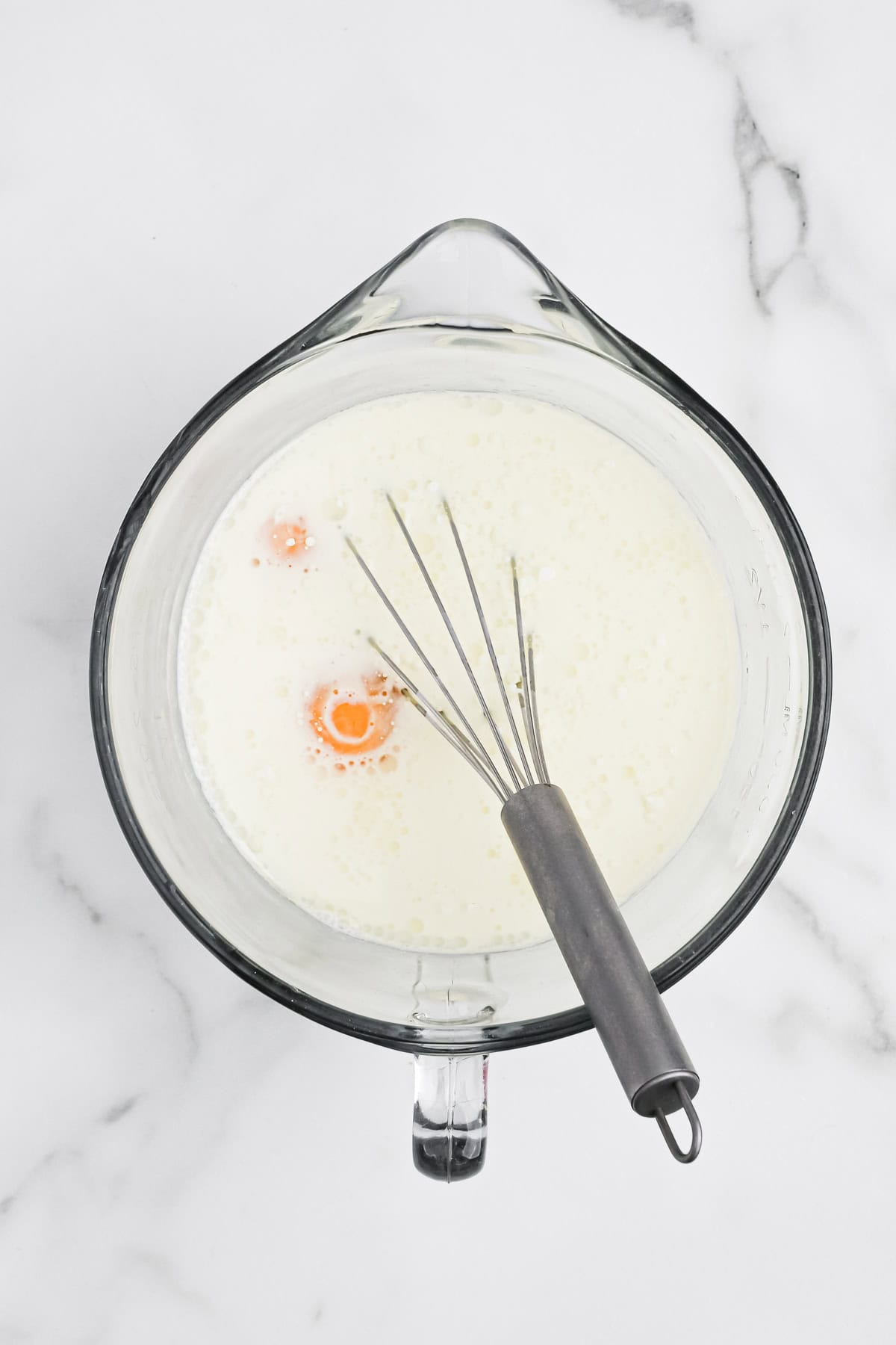 Eggs and milk whisked together in a mixing bowl on white counter