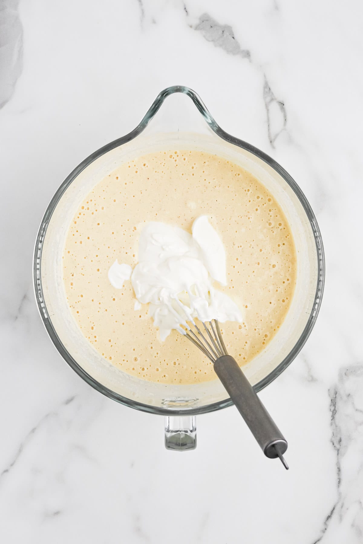 Sour cream added to traditional cornbread batter on white countertop with a whisk