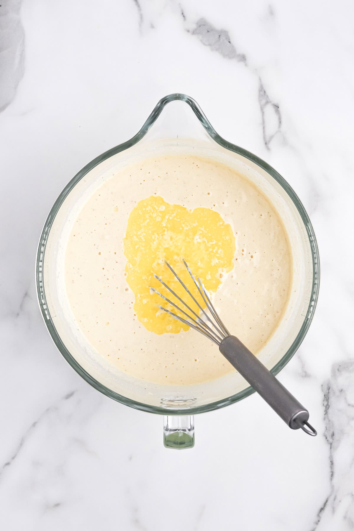 Melted butter added to cornbread batter in clear bowl on white background