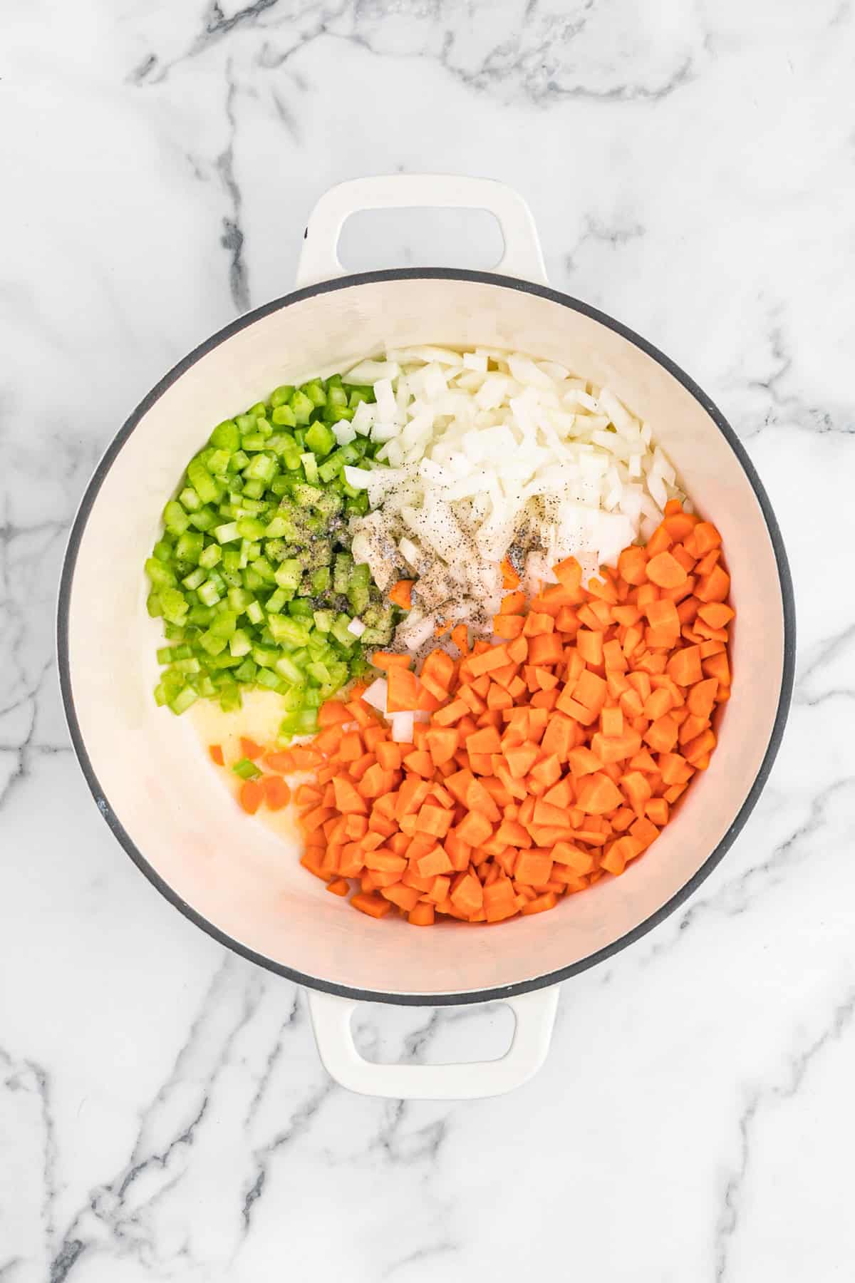 Carrots, celery and onions chopped with seasoning in a pot with butter on white countertop