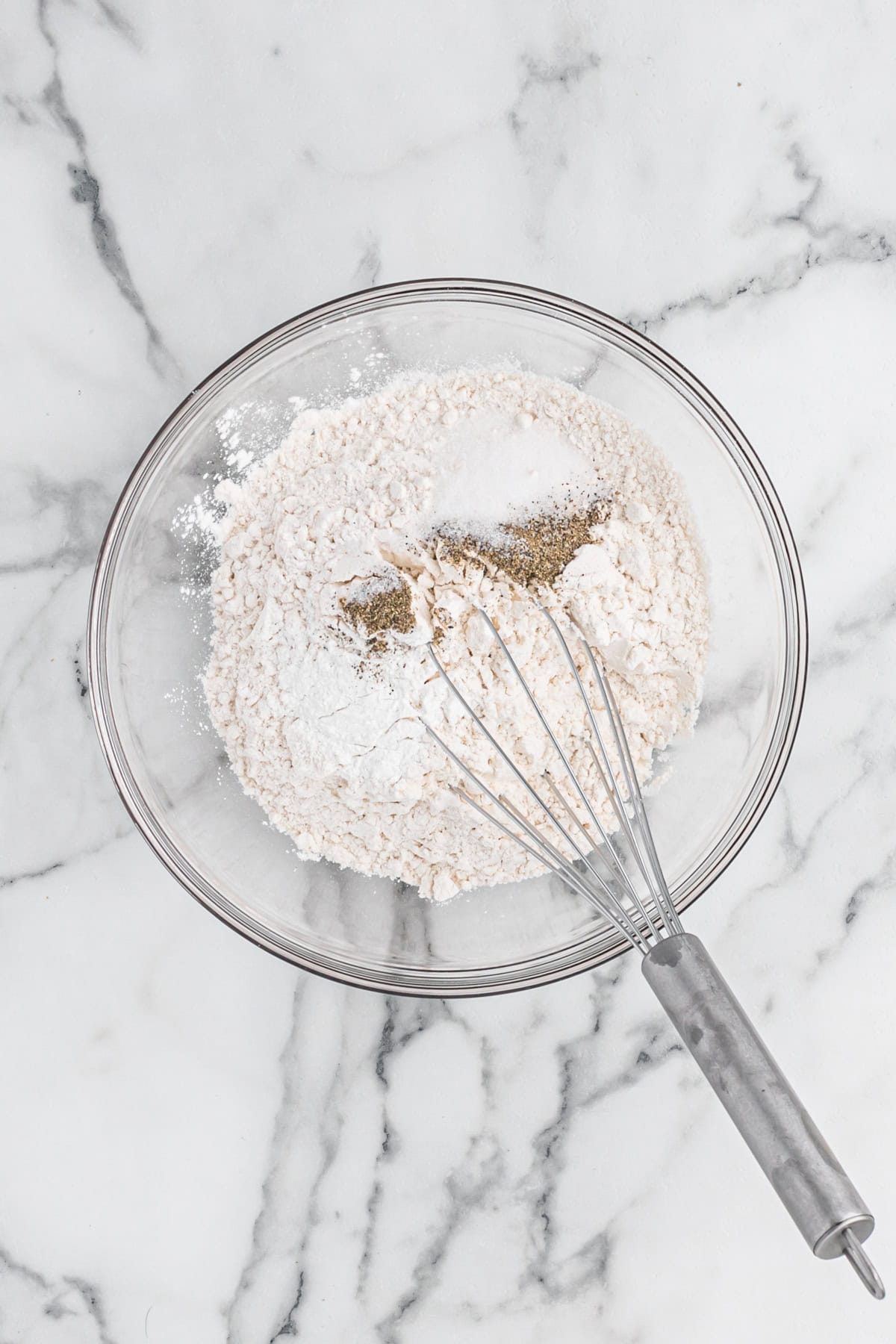 Dry ingredients being mixed in a glass bowl on white countertop