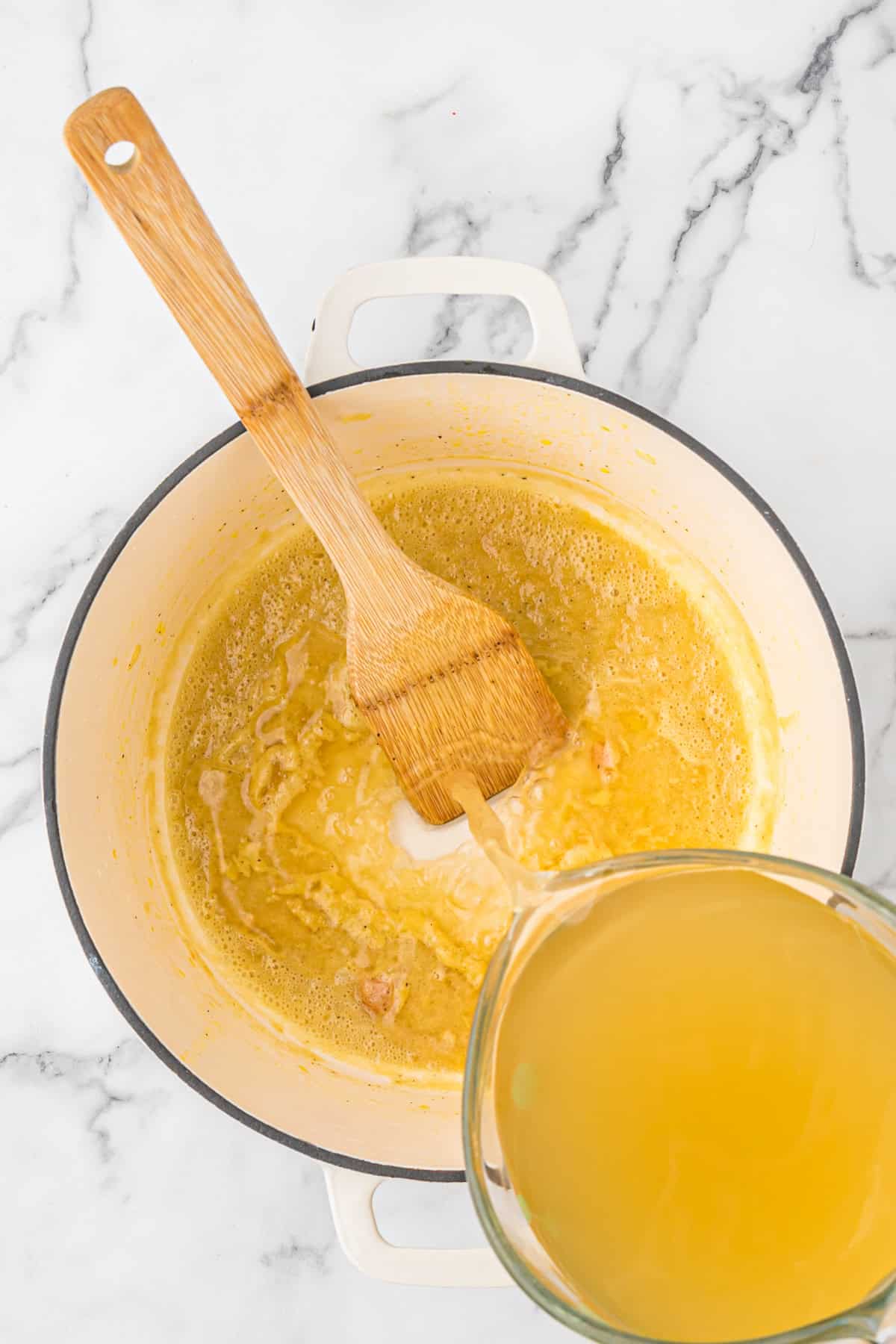 Whisk being added to a large white pot mixing on white countertop