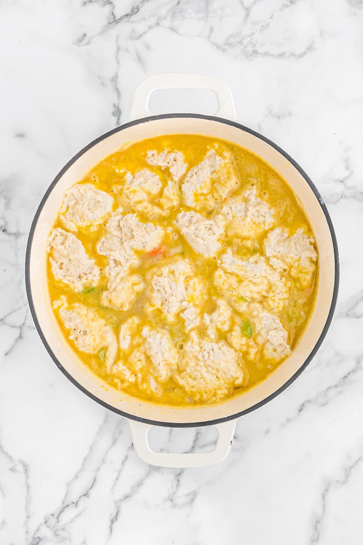 Dumpling dough dolloped over chicken stew in white pot on white countertop